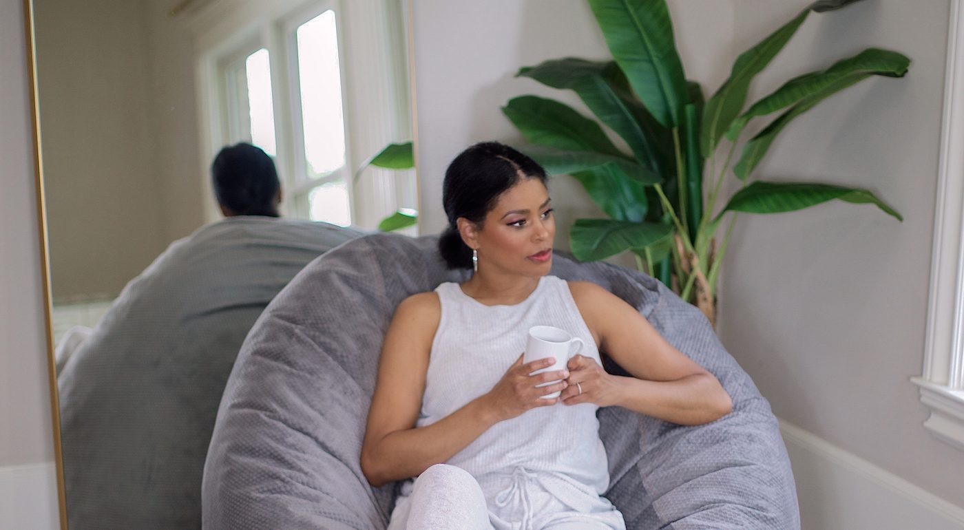 A woman relaxing with a mug in a gray CordaRoy’s beanbag chair